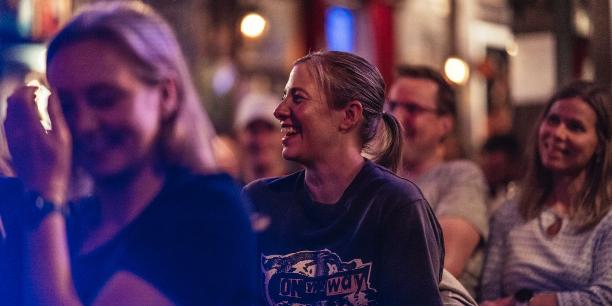 Kvinne som ler og koser seg på standupshow i Oslo i regi av Reis deg komikerklubb