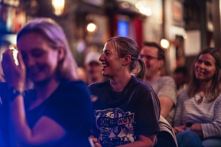 Kvinne som ler og koser seg på standupshow i Oslo i regi av Reis deg komikerklubb